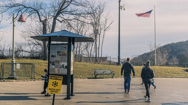 Visitors on a cold, windy day walk past an information kiosk & ice warning sign