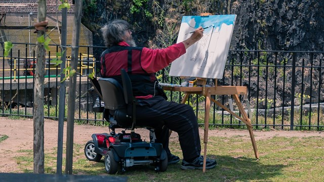 A man in a power wheelchair paints the Great Falls with a large easel