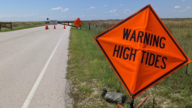 A orange road sign that says warning high tides. 