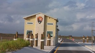 Park entrance station with the NPS arrowhead on it and a sky with clearing clouds.