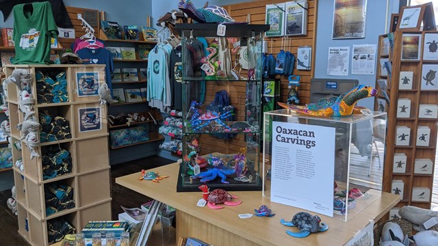 Inside of store with various items of merchandise including shirts and carved wooden figures