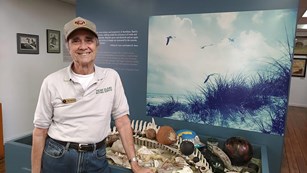 A volunteer smiles at the camera as he stands in front an exhibit in the visitor center.
