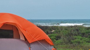 Orange tent pitched in front of dunes with Gulf of Mexico in background