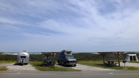 Campsites with trailers and tents, picnic tables with shelters, and the gulf just barely visible
