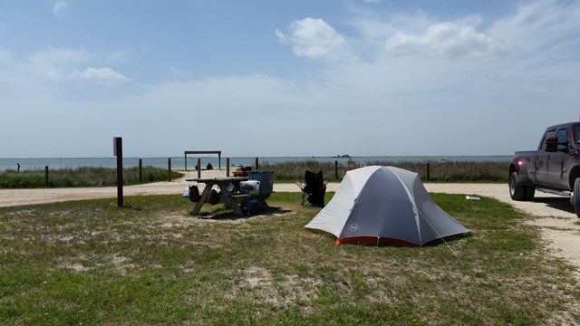 A tent pitched on a grassy area next to a picnic table with the laguna just barely visible.