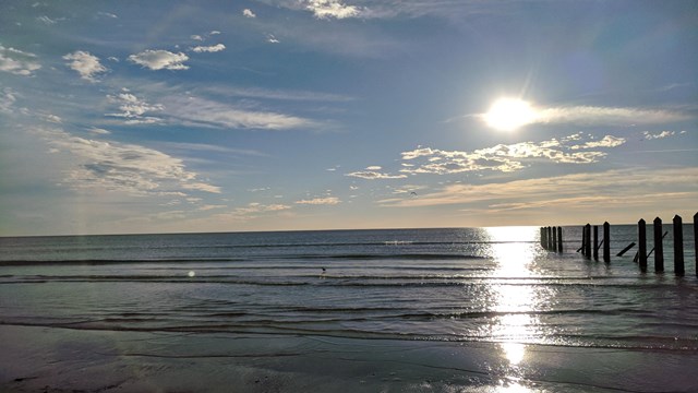 The ocean with the sun reflecting and shining on it.  Bollards are visible on the right.