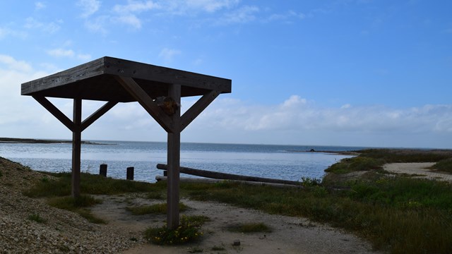 A shade structure on the shore with the calm waters of the laguna behind.