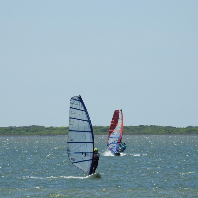 Two people windsurfing on calm water.