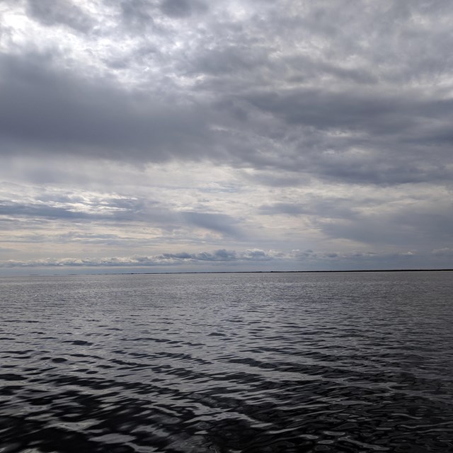 Calm water stretches to the horizon with a cloudy sky above.