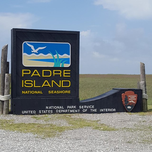 Park entrance sign with simple painting of bird flying over the beach.