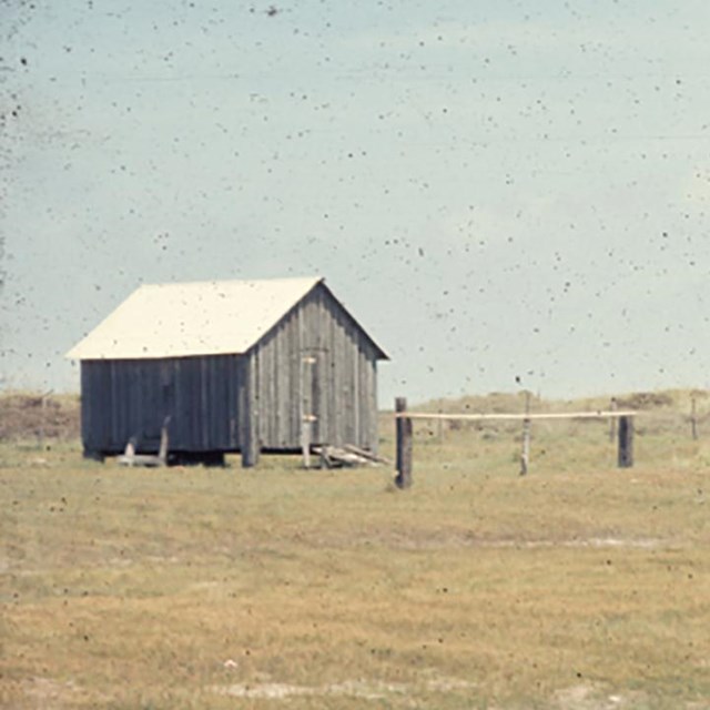 An old, grainy photograph of a few small wooden buildings in the grasslands.