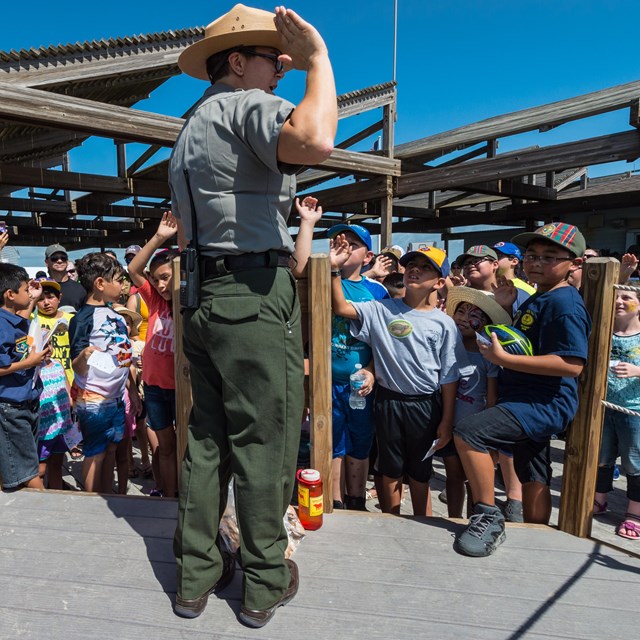 A ranger stands in front of a crowd of kids with right arms raised in pledge.