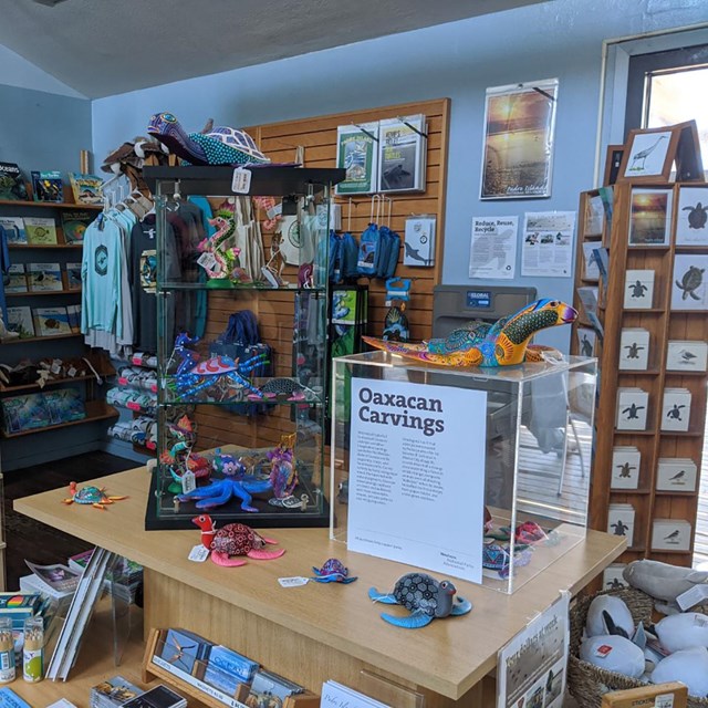 Inside of store with various items of merchandise including shirts and carved wooden figures