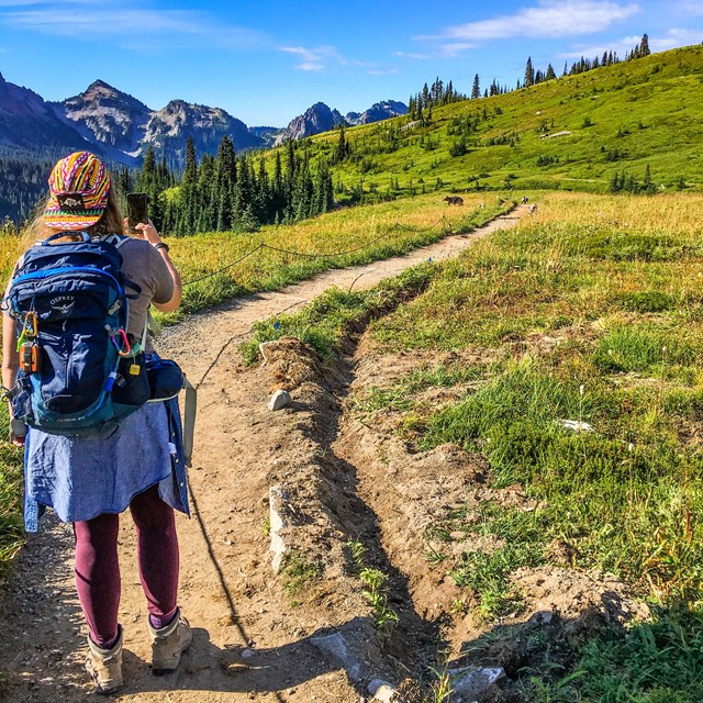 a hiker takes a photo with her phone while hiking on a trail in the mountains