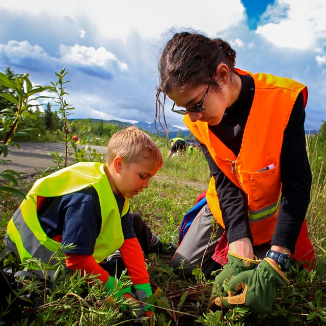 a young boy and girl in safety vests pull weeds