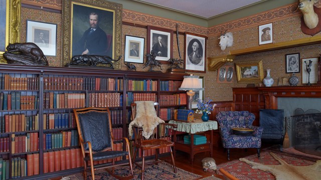 A living room covered with oriental carpets and patterned orange, brown, and green wallpaper.