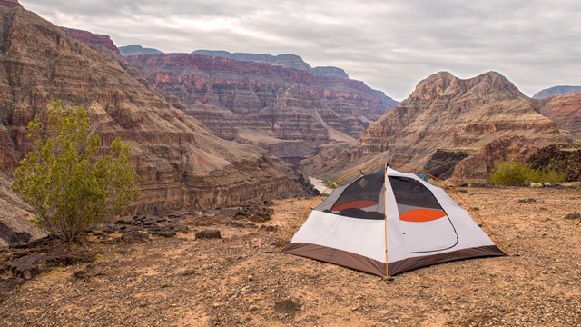 View of a single backpacker's tent near the edge of a scenic viewpoint overlooking Whitmore Canyon. 