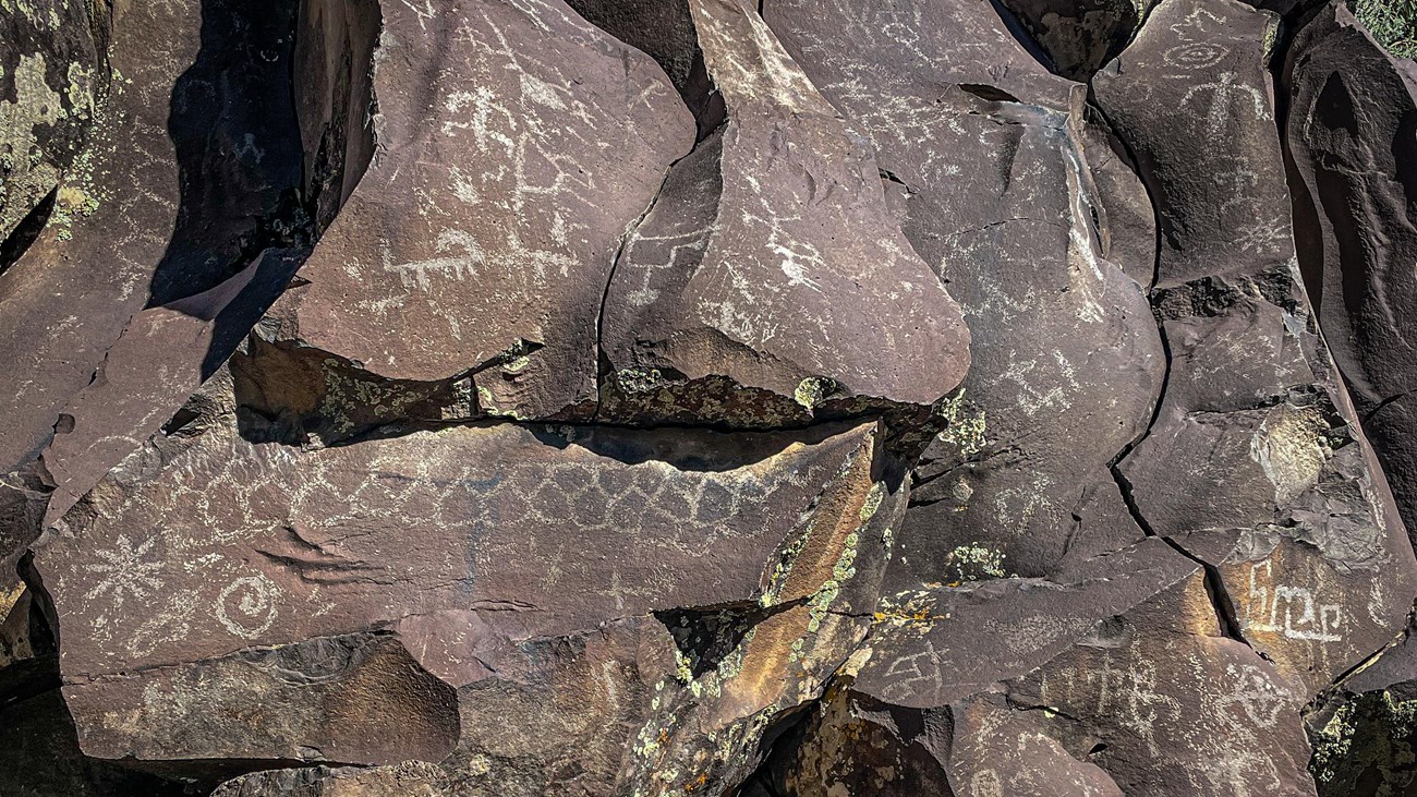 Native American rock writing at Nampaweap. Images are carved into dark basalt rock.