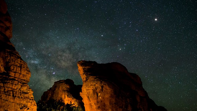 View of the Milky Way with red rocks lit up in the foreground. 