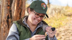 Uniformed woman holds a black, orange, and white bird with wing spread out. NPS/Jacob W. Frank