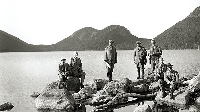 historic black and white image of a group of men on a rock outcropping by a lake