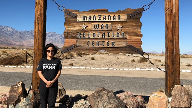 A woman stands next to a sign that says Manzanar War Relocation Center