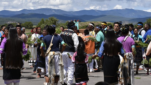 Many people standing in front of blue mountains and cloudy blue skies. 