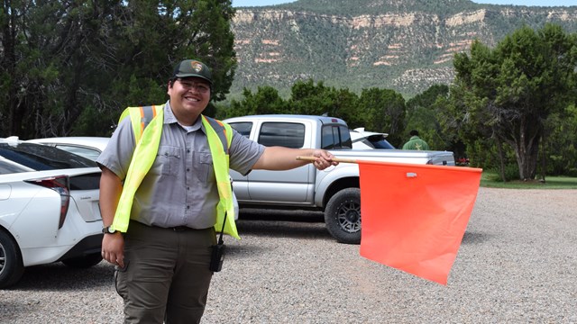 Park employee holding out orange flag in parking lot