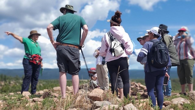 A park volunteer in green points out of the frame while a group of visitors stands listening