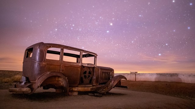 an old, abandoned car sits beneath a starry purple sky.
