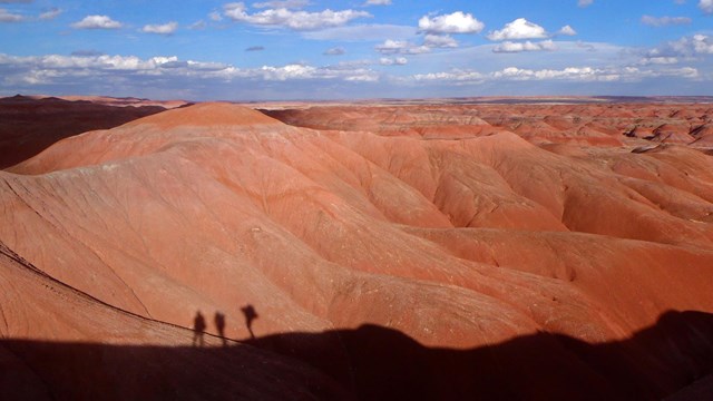 Hikers on a ridge cast shadows on red buttes.