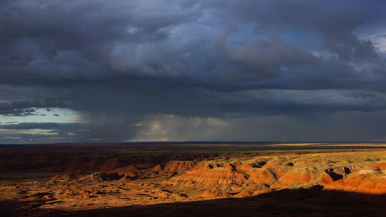 Dark thunderheads above sunset lit badlands.