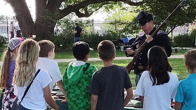 Photo of a National Park Rangers talking to kids in living history clothing.