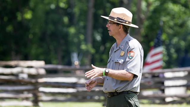 Photo of a National Park Rangers in a ranger hat and ranger rain coat talking about the battle. 