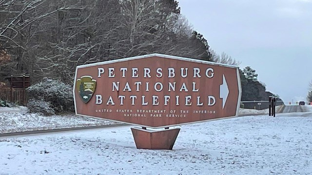Entrance sign text reads Petersburg National Battlefield stand on snow covered ground.