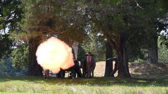 Looking toward a cannon as it fires - large billow of yellow smoke illuminates a cannoneer.