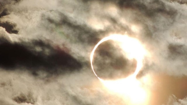 An annular eclipse distorted behind light cloud cover.