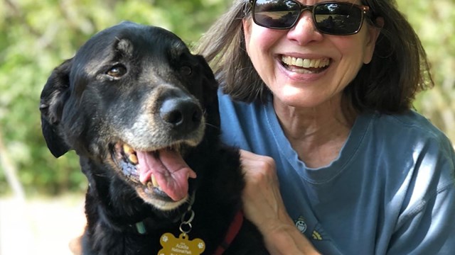 Woman smiles with black dog wearing tag.
