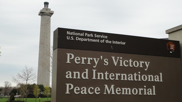 A rectangular brown sign with the Memorials name and a black stripe across the top.