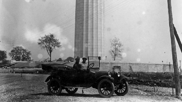 Black & white photo with visitors in a car in front of Memorial.