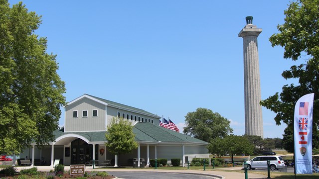 Circle drive in front of a tan building with a green roof and memorial column rising in the blue sky