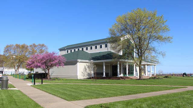 A white building with a two story center that is all glass surrounded by a deck with white pillars 