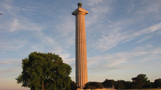 Sea wall retains water in front of the Memorial column under a blue sky with clouds 