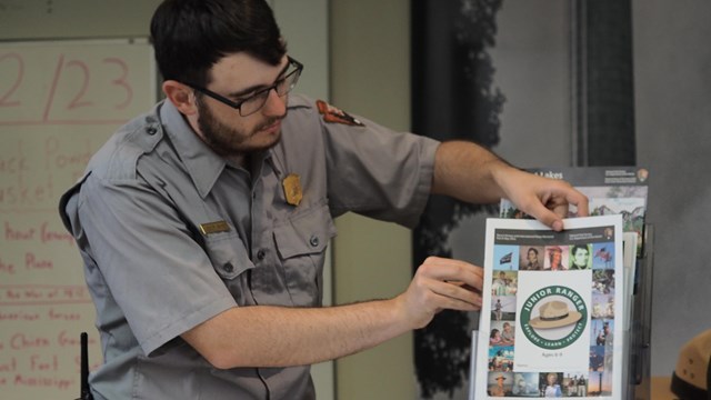 NPS Park Ranger fills a counertop display with Junior Ranger Books 