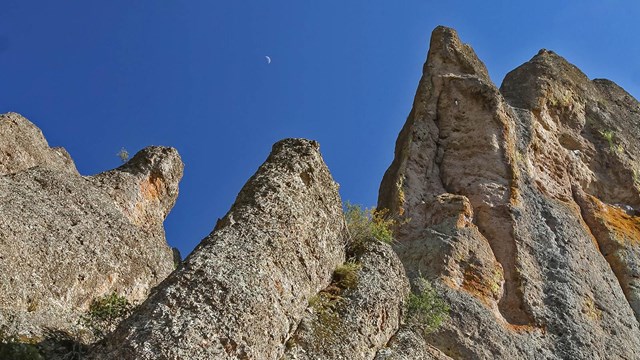 Rocky peaks set against a clear blue evening sky with a sliver of moon.