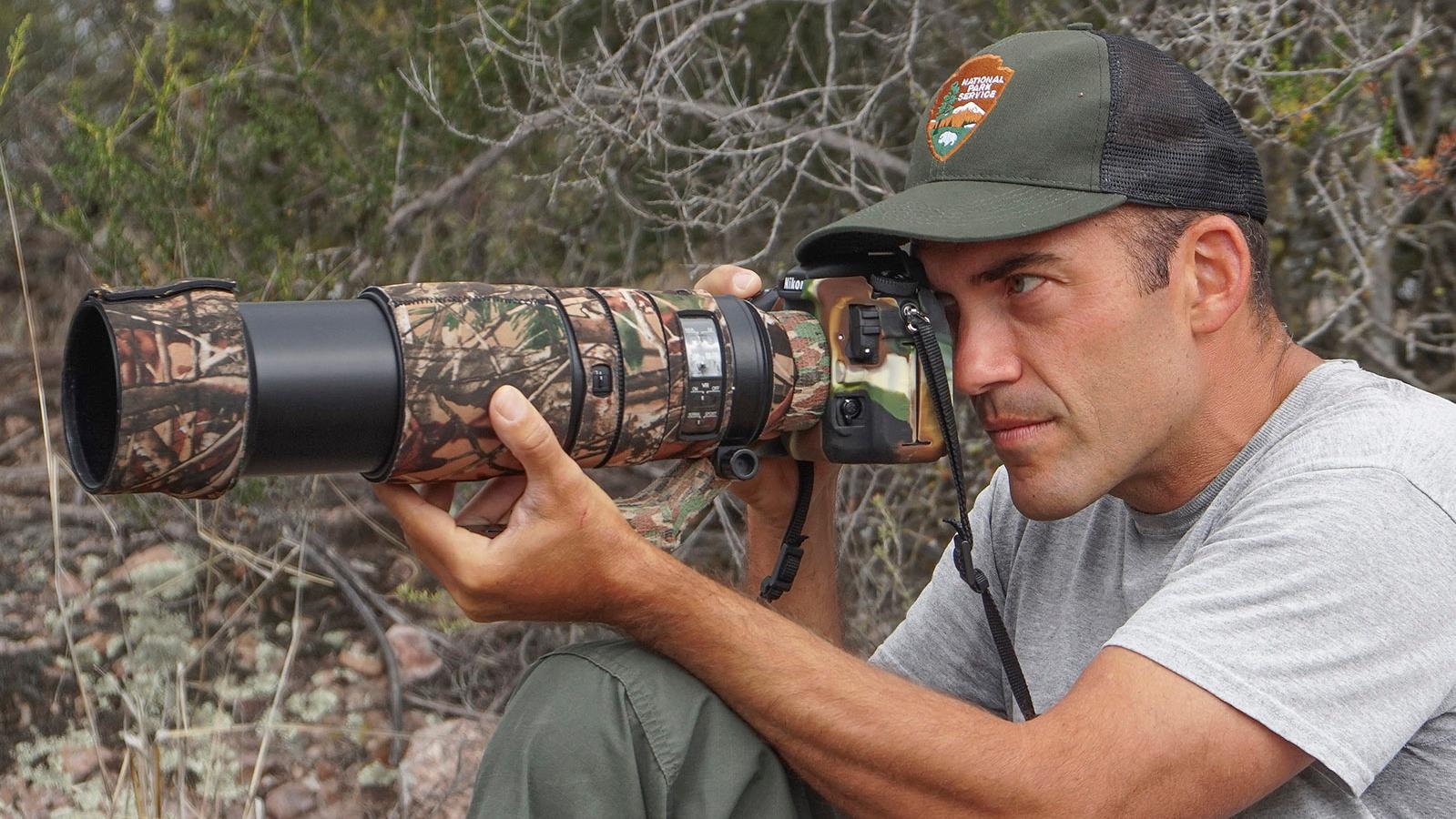 Candid of biologist in National Park Service hat aiming a camera lens.