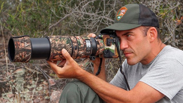Candid of biologist in National Park Service hat aiming a camera lens.