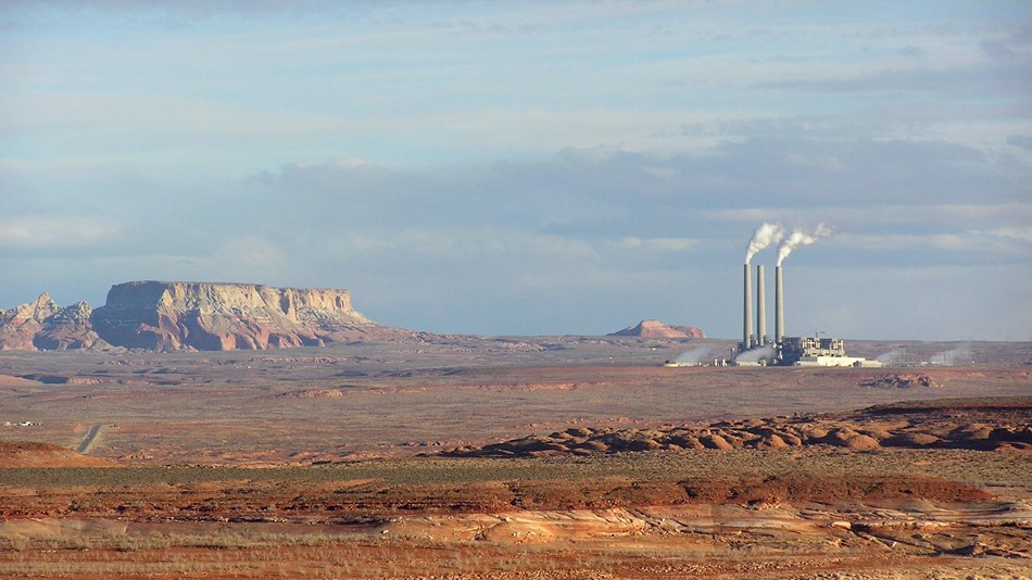 Landscape photo of rock formations and factory pipes with smoke coming out.