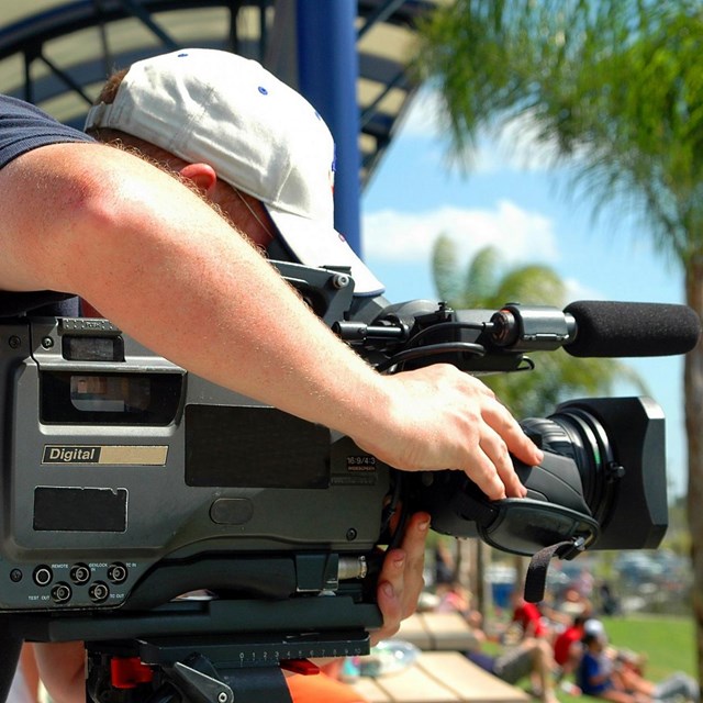 A man with a large video camera outdoors