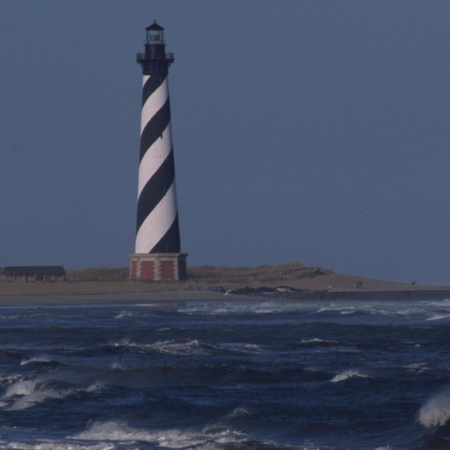 ocean in front with black and white lighthouse in distance